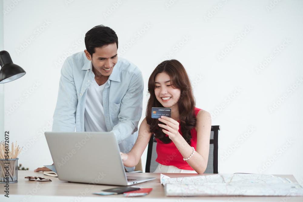 Travel concept, Happy Asian young couple using a laptop and booking hotel online with a credit card, woman holding passports with tickets, prepare to travel Travel concept, Happy Asian young couple using a laptop and booking hotel online with a credit card, woman holding passports with tickets, prepare to travel