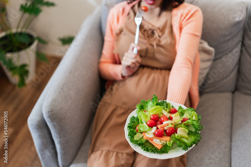 Happy pregnant Asian woman sitting and eating natural vegetable salad healthy food and sitting on sofa © ronnachaipark