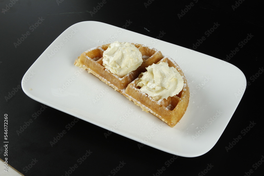 Waffle with whipped butter and powdered sugar on a black background