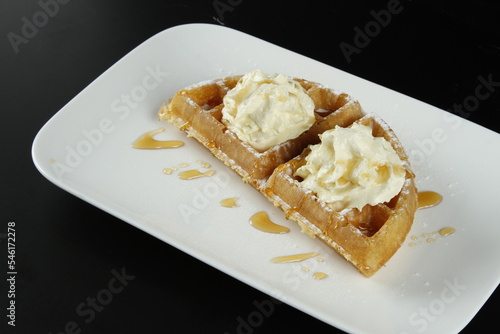 Waffle with whipped butter and powdered sugar on a black background