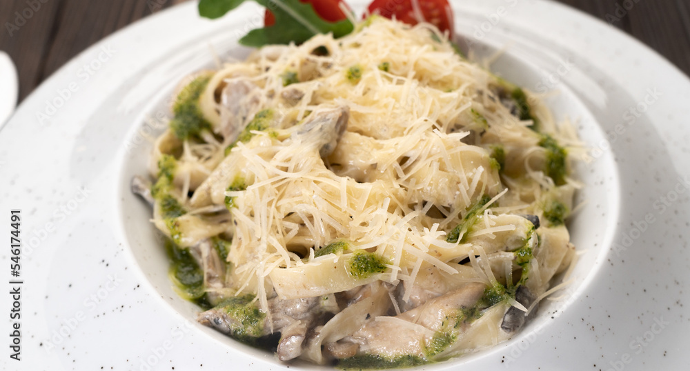 Plate of Italian creamy pasta with chicken and mushrooms decorated with basil sauce. Traditional Italian lunch