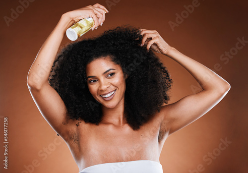 Hair care, afro and spray with wellness, cosmetic and happy smile against a brown studio background with mockup. Happiness, health and care for curls with beauty, natural or luxury cosmetics product