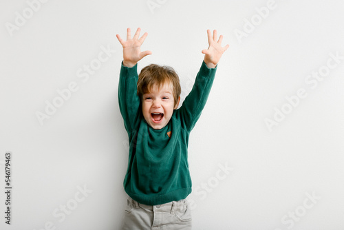 Cute little boy with raised hands up with happiness on white wall background
