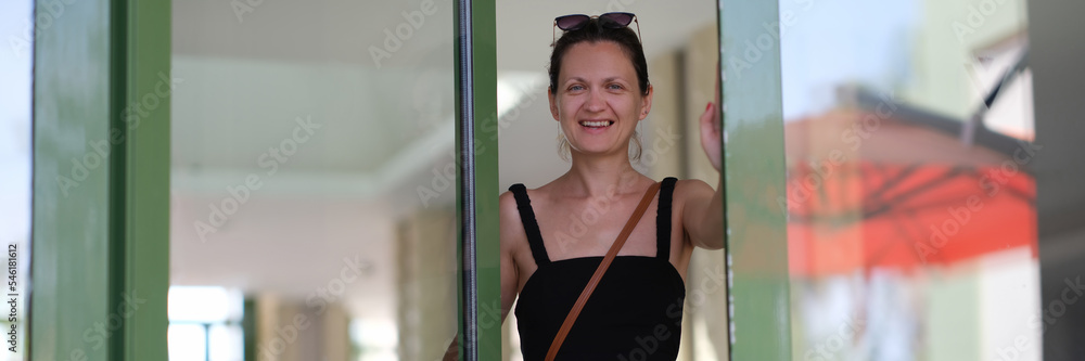 Young smiling woman in black dress entering glass door