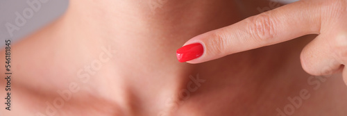 Woman with red manicure pointing finger at neck area with thyroid gland closeup photo