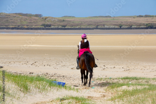 Young woman and her bay horse ride on to the beach in Anglesey Wales happy to enjoy the empty beach and the freedom to move fast that it will allow them. 