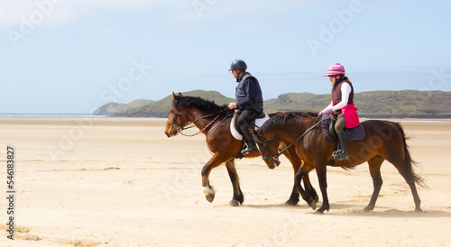 Father and daughter enjoying horse riding together on beach in Anglesey Wales.Horses enjoying the freedom to move on beach people enjoying living the dream, riding together at the seaside.