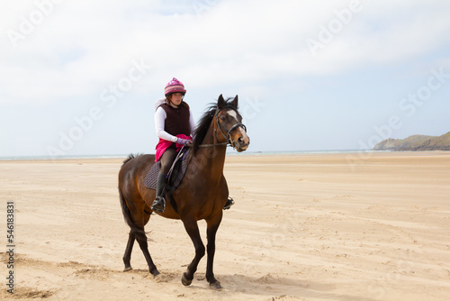 Pretty young rider and her horse enjoy the freedom that riding on large empty beach gives them.Rider wearing pink on bay horse, horse looks alert and ready to run.