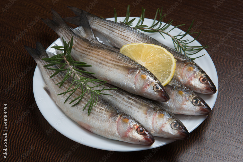 Several fresh mullet fish on a white plate, with sprigs of rosemary and a slice of lemon Several fresh mullet fish on a white plate, with sprigs of rosemary and a slice of lemon