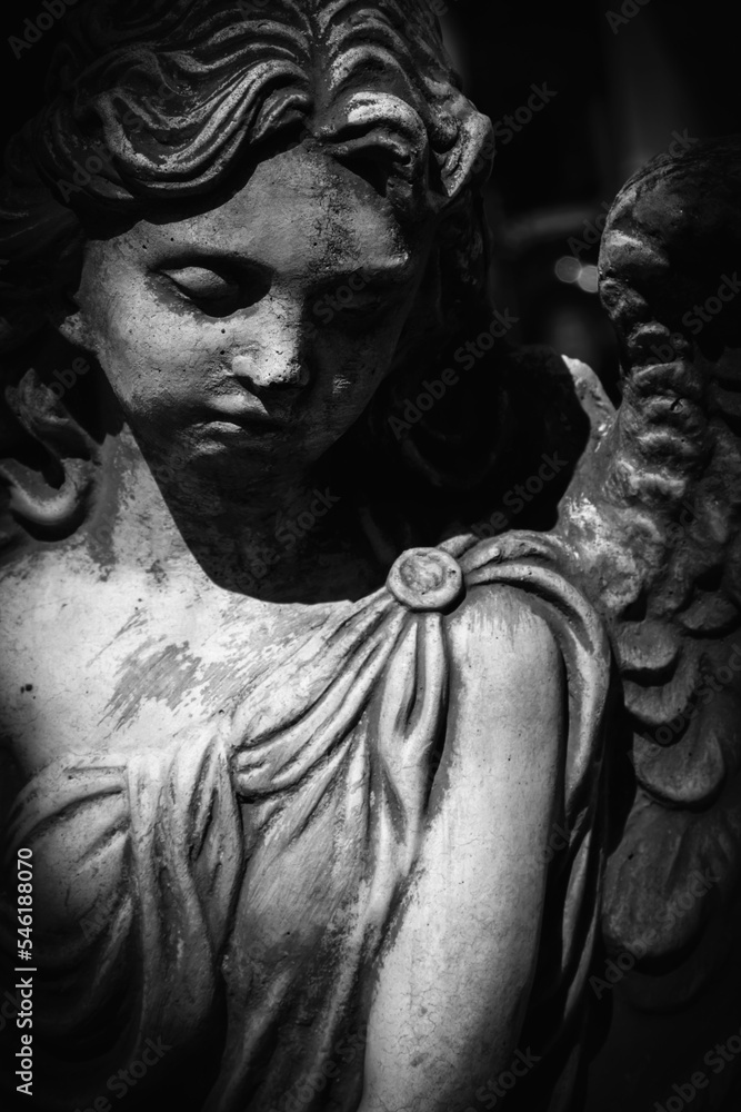 Black and white vertical image of sad angel of death. Fragment of an ancient statue.