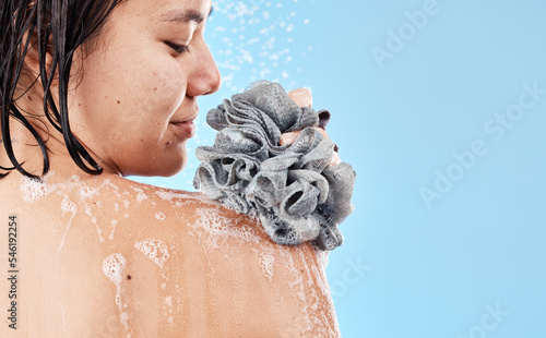 Shower, sponge and woman cleaning body with water, soap foam and skincare for wellness, personal hygiene and cosmetics on mockup studio blue background. Asian girl model, beauty and bath with loofah photo