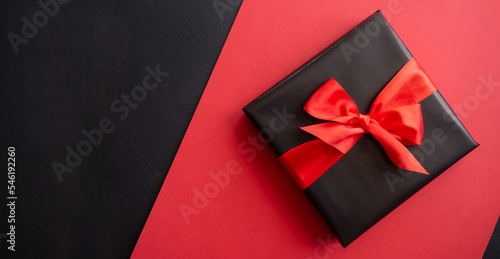 Gift box wrapped in black paper with a red bow. Red, black background. Holiday concept. Place for text or advertising. Christmas. Valentine's Day.