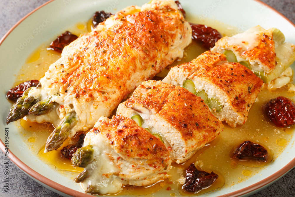 Chicken meat stuffed with fresh asparagus, mozzarella cheese and sun-dried tomatoes served with fragrant sauce close-up in a plate on the table. Horizontal Chicken meat stuffed with fresh asparagus, mozzarella cheese and sun-dried tomatoes served with fragrant sauce close-up in a plate on the table. Horizontal