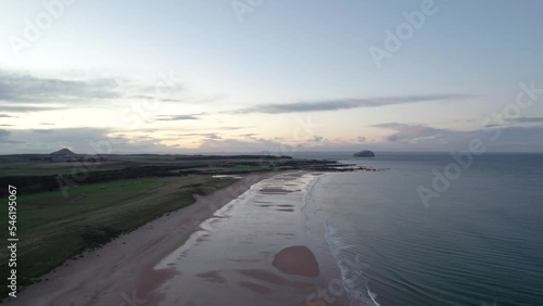 Stationary drone footage flying high above a long sandy beach at sunset looking out across the rippling ocean as the tide gently laps the shore. Tyninghame Beach, Scotland photo