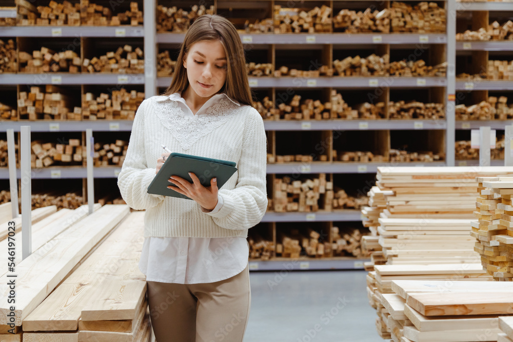 Woman with tablet in a timber and lumber warehouse. Product acceptance and quality control