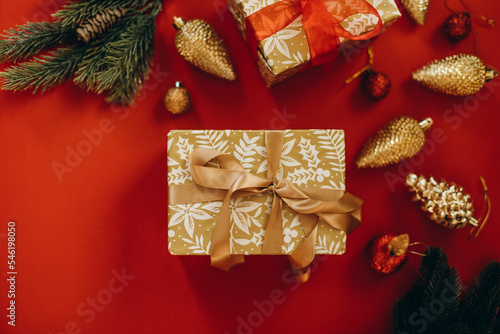 two gift boxes on a red background with Christmas decorations and fir branches. christmas gifts decorated with beige and red ribbon.