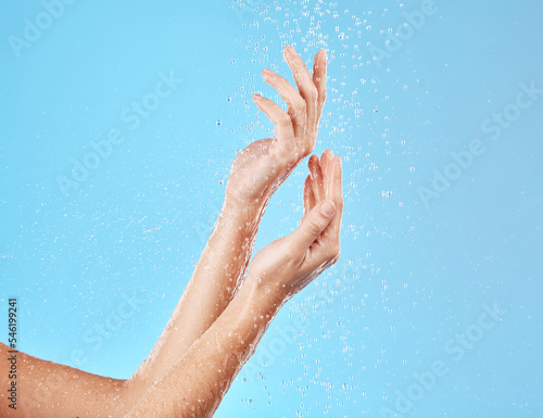 Hand, water and cleansing for health, wellness and bodycare on a blue studio background. Hands, fingers and shower cleaning of body and arms for cleansing, hygiene and grooming flow