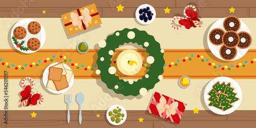 Vector illustration of festive New Year's table top view. Delicious Christmas feast with cookies, toast, donuts by candlelight and Christmas wreath on cartoon style.