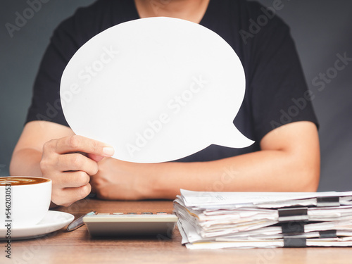 Close-up of a hand holding a blank white speech bubble while sitting at the table in the office