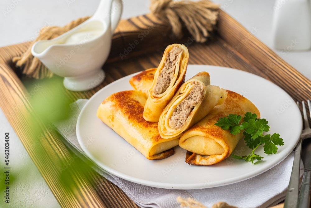 Thin pancakes stuffed with boiled minced meat with fried onions on a white plate on a light concrete background. Pancake recipes. Thin pancakes stuffed with boiled minced meat with fried onions on a white plate on a light concrete background. Pancake recipes.