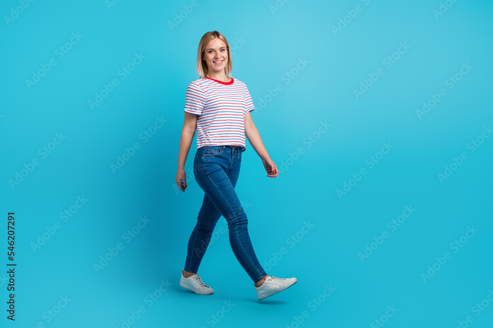 Full length photo of pretty friendly woman dressed t-shirt smiling walking isolated blue color background Full length photo of pretty friendly woman dressed t-shirt smiling walking isolated blue color background