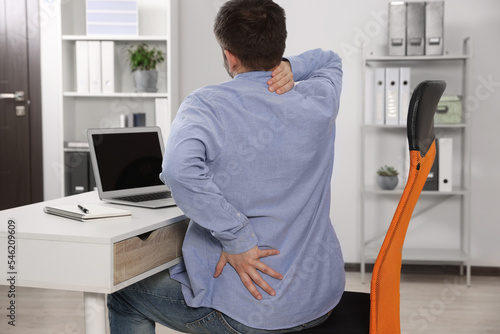 Man suffering from back pain while working with laptop in office. Symptom of scoliosis