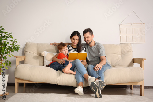 Happy family reading book together on sofa in living room at home