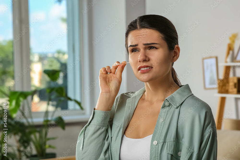 Young woman cleaning ear with cotton swab in room Young woman cleaning ear with cotton swab in room