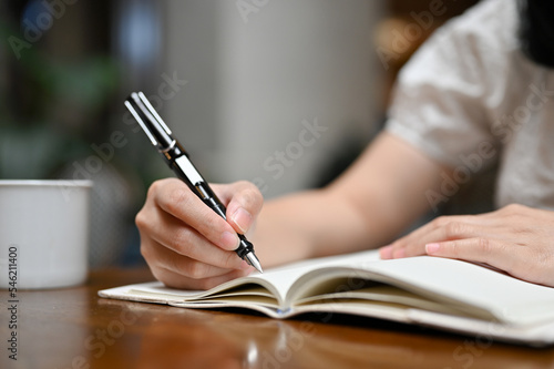 Young Asian woman writing something on her notebook, holding pen. writing, taking notes, listing.
