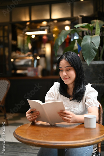 Attractive young Asian female reading a book while relaxing in the beautiful coffee shop.