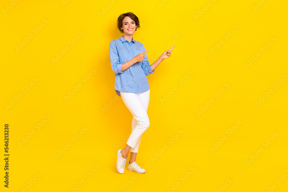 Full length photo of positive pretty lady wear blue shirt pointing two fingers empty space isolated yellow color background Full length photo of positive pretty lady wear blue shirt pointing two fingers empty space isolated yellow color background