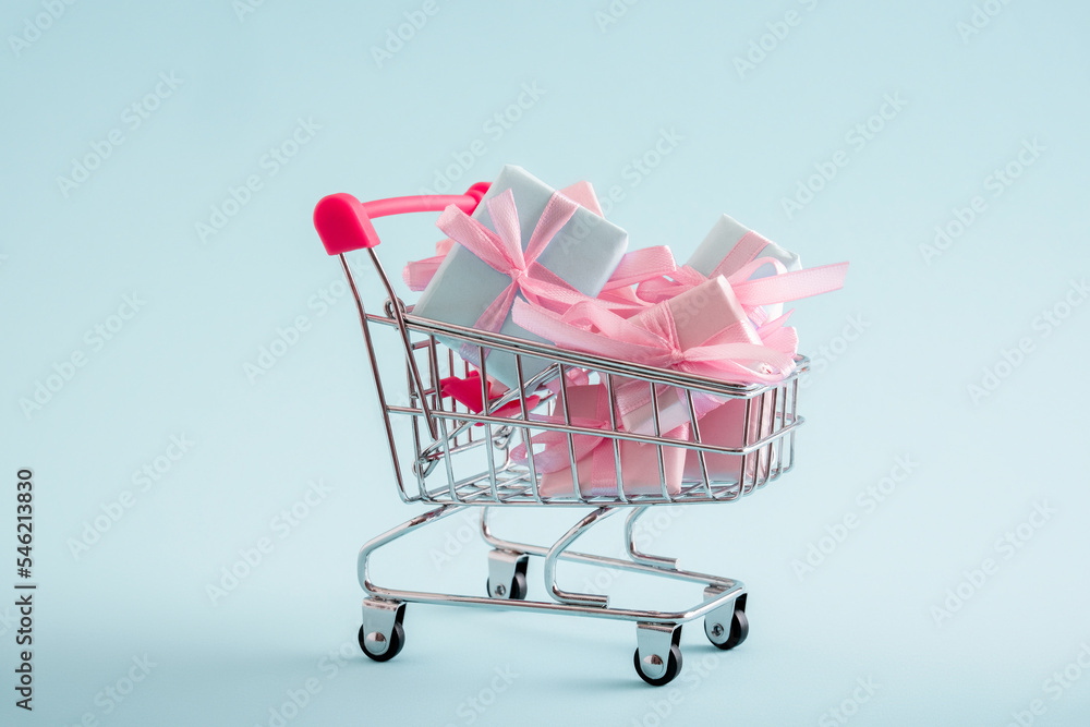 Shopping cart full of present boxes on a blue pastel background. Copy space. Minimal shopping concept. Shopping cart full of present boxes on a blue pastel background. Copy space. Minimal shopping concept.