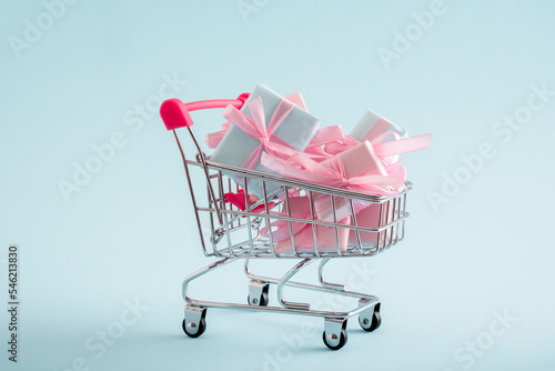 Shopping cart full of present boxes on a blue pastel background. Copy space. Minimal shopping concept.