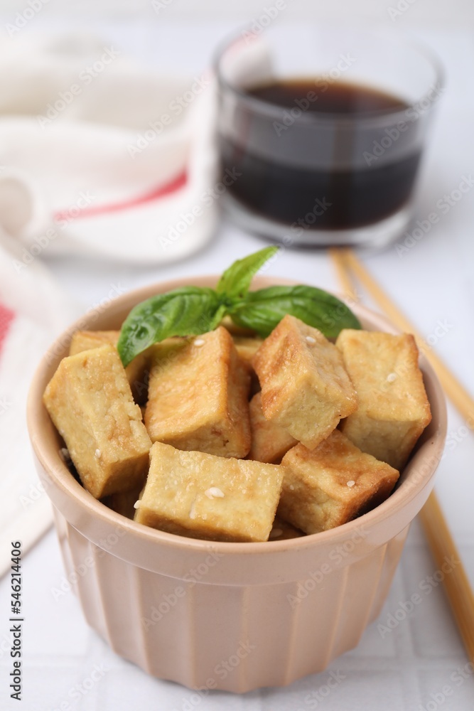 Delicious fried tofu with basil and sesame seeds in bowl on white tiled table Delicious fried tofu with basil and sesame seeds in bowl on white tiled table