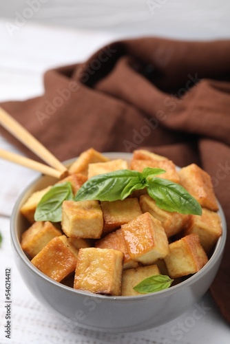 Bowl with delicious fried tofu and basil on white table