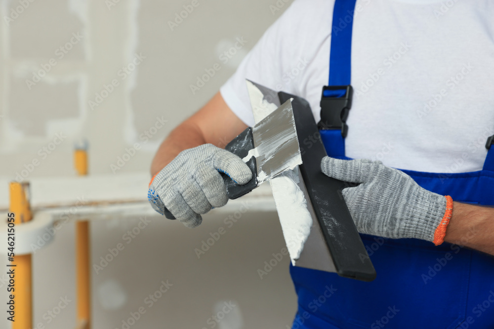 Worker with putty knives and plaster near wall, closeup Worker with putty knives and plaster near wall, closeup