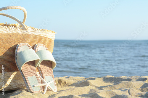Straw bag, slippers and dry starfish on sandy beach near sea, space for text