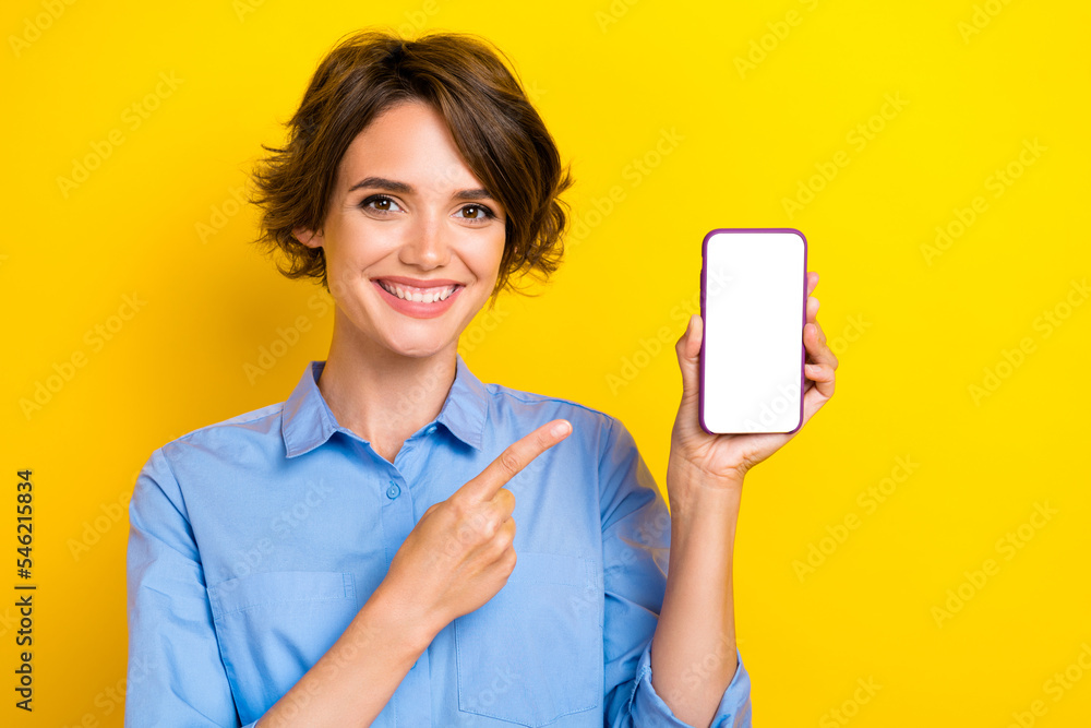 Photo of cheerful nice girl with brown hair dressed blue shirt directing at phone app advertising isolated on yellow color background Photo of cheerful nice girl with brown hair dressed blue shirt directing at phone app advertising isolated on yellow color background