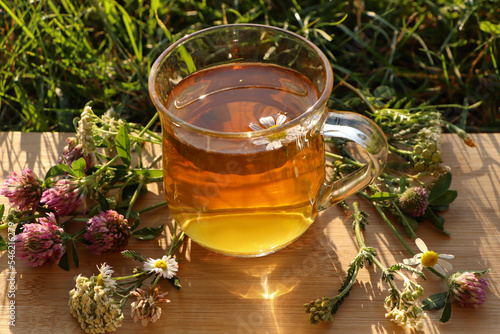 Cup of aromatic herbal tea and different wildflowers on green grass outdoors