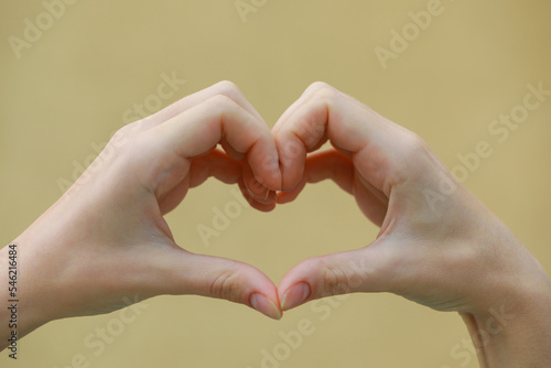 Woman making heart with hands on beige background  closeup
