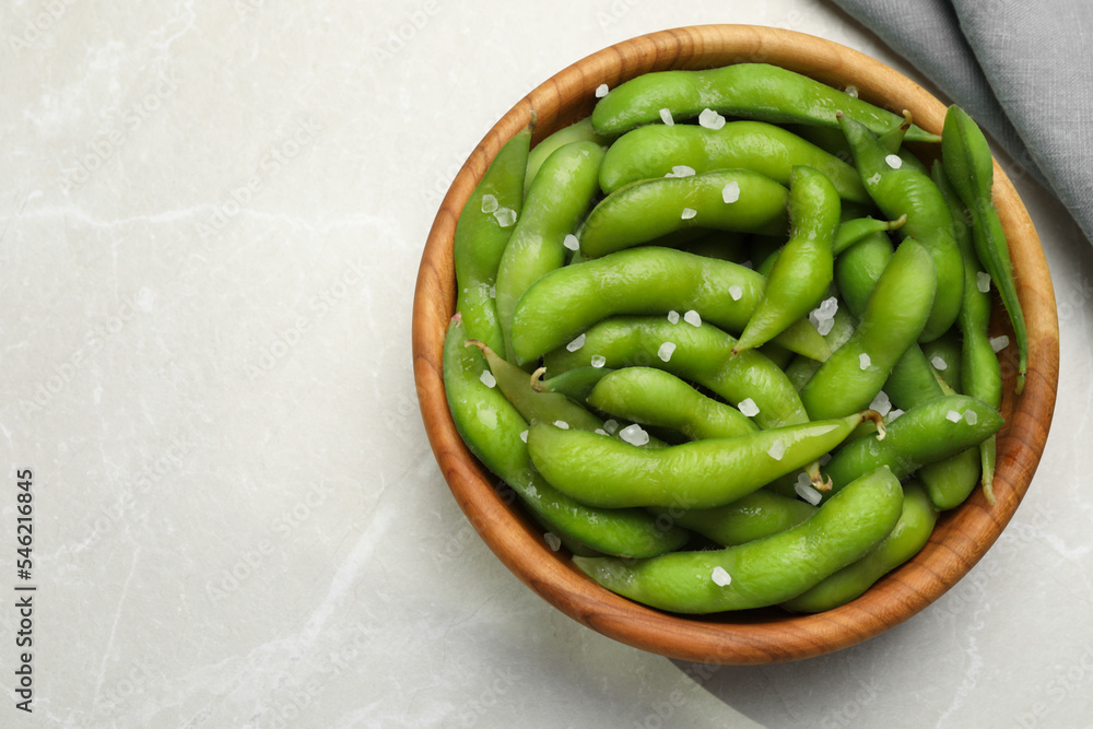 Bowl of green edamame beans in pods with salt on light grey table, top view. Space for text Bowl of green edamame beans in pods with salt on light grey table, top view. Space for text
