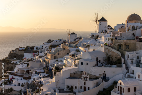  Whitewashed houses and windmills in Oia in warm rays of sunset on Santorini island. Greece