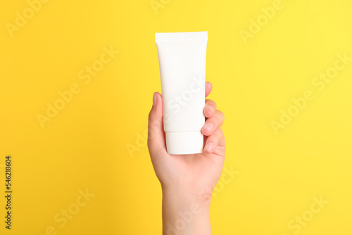 Woman holding tube of face cream on yellow background, closeup