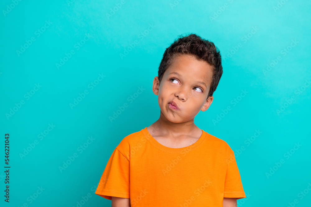 Photo of funny doubtful little guy dressed orange t-shirt looking empty space isolated teal color background Photo of funny doubtful little guy dressed orange t-shirt looking empty space isolated teal color background