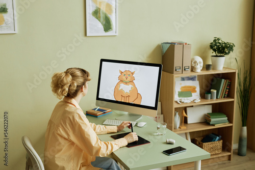 Desktop computer with fat ginger cat drawn by young creative digital artist on screen during work over new collection of graphic pictures