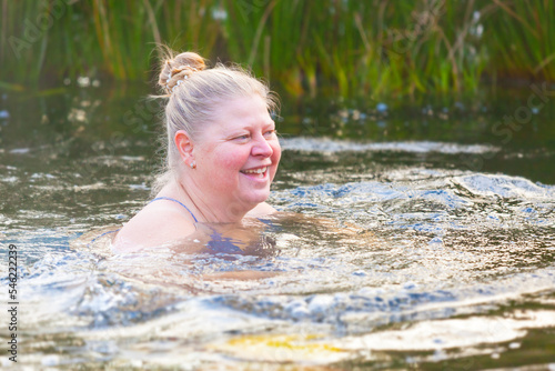 An elderly woman swims in the cool water of a garden pond. Hardening is her lifestyle. Adventure is ageless.