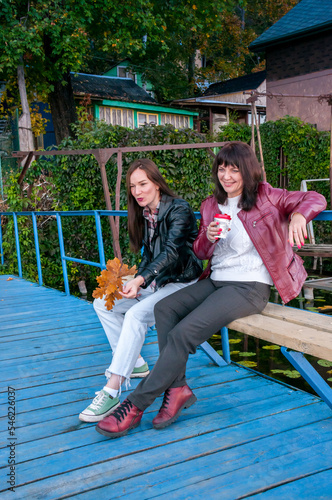 Two brunette women are sitting on a bench and chatting in the fall