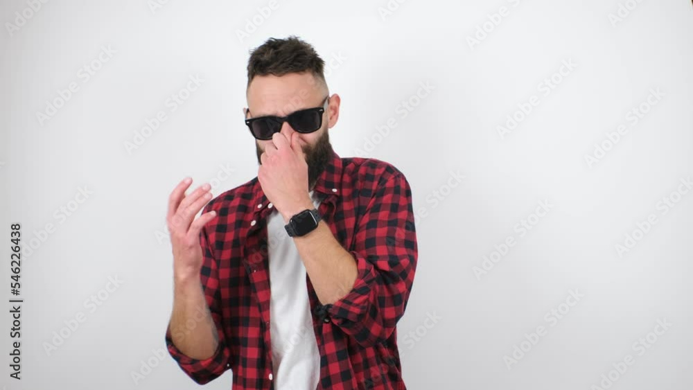 Dissatisfied bearded hipster guy pinches his nose, holding his breath, expressing disgust at the bad smell. The video was shot in a studio on a white background. Dissatisfied bearded hipster guy pinches his nose, holding his breath, expressing disgust at the bad smell. The video was shot in a studio on a white background.
