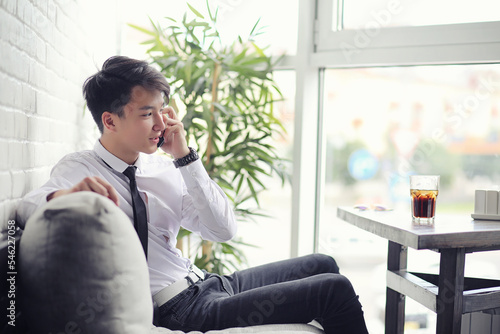 A young Asian businessman is waiting for a partner in a cafe. Business meeting in the restaurant. A Korean young man talking on the phone in a cafe.