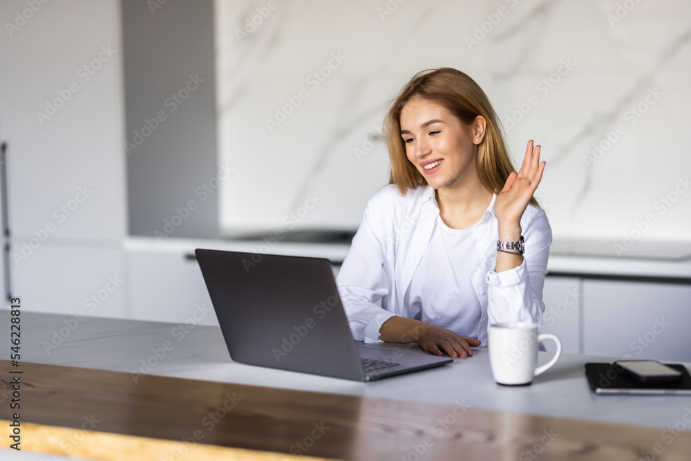Smiling young woman making video call and heaving a breakfast in her kitchen. Smiling young woman making video call and heaving a breakfast in her kitchen.